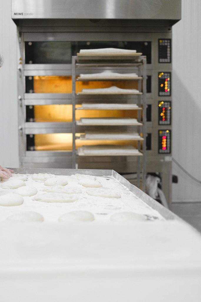 Industrial bakery scene with dough preparation and multi-shelf oven heating.